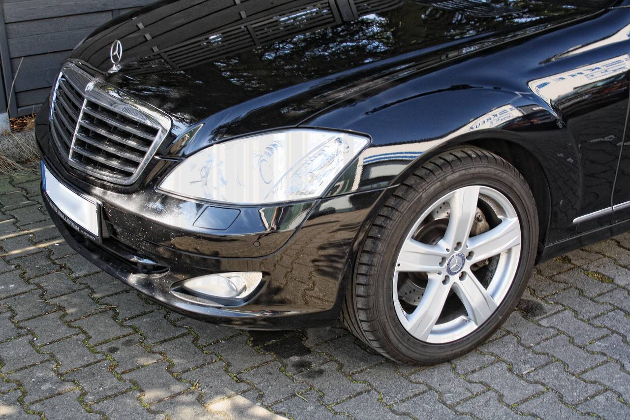 Parte anteriore di una limousine nera, parcheggiata su un piazzale lastricato, con il logo Mercedes ben visibile sul cofano.