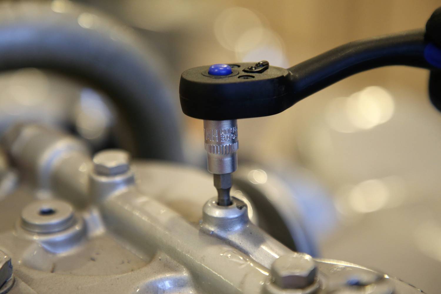 Chiave inglese che avvita un bullone sul motore. Un primo piano mostra il processo di fissaggio in un ambiente di officina.