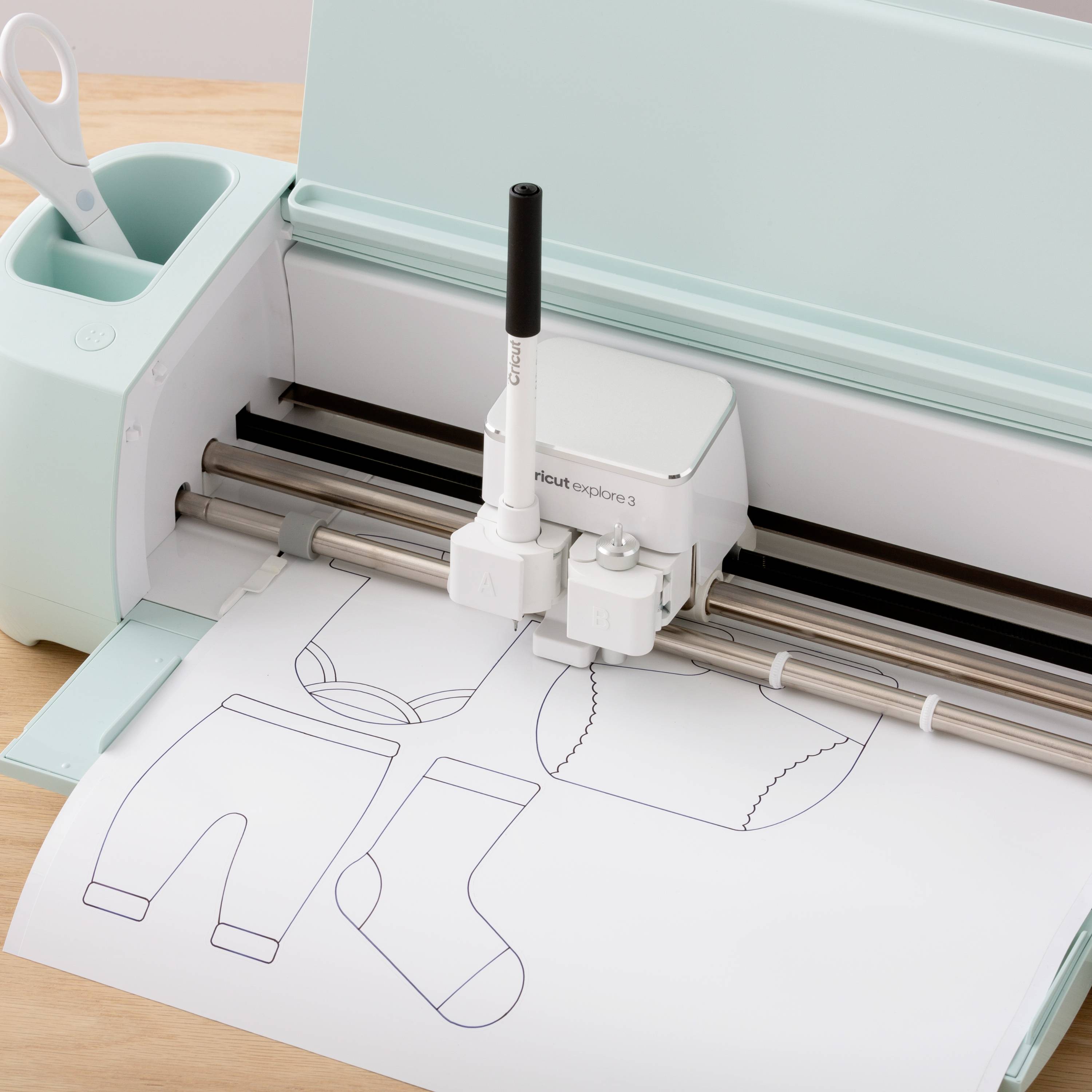 Un dispositivo elettrico da taglio ritaglia motivi per abiti per bambini su carta. Accessori e carta su un tavolo di legno.