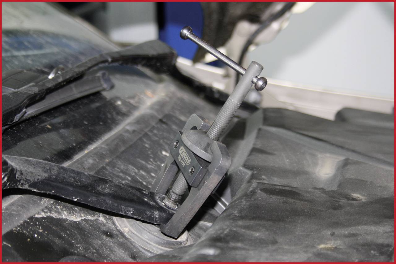 Un attrezzo estrattore è fissato a un componente dell'auto per rimuoverlo. L'auto e l'attrezzo sono ricoperti di polvere.