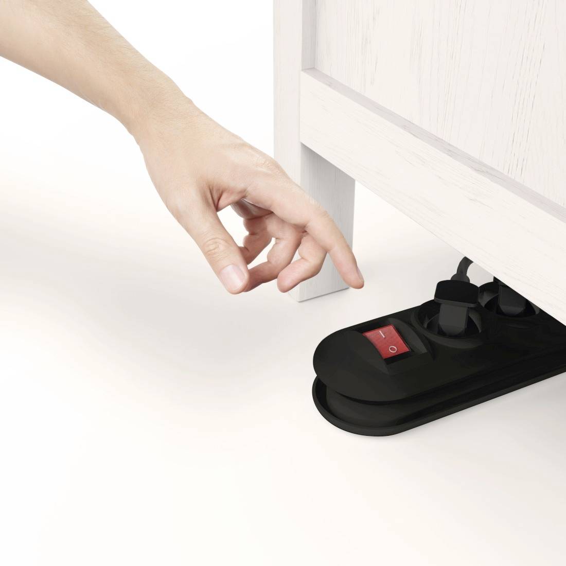 Una mano spegne una multipresa sotto un mobile in legno. Due spine sono inserite nella presa multipla.