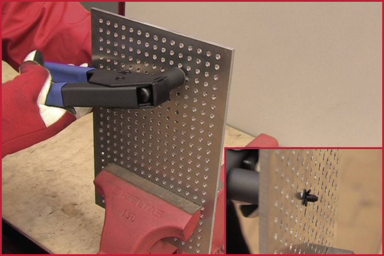 Una persona con guanti rossi sta utilizzando un utensile per inserire un rivetto a strappo in una lamiera metallica forata, fissata in una morsa.