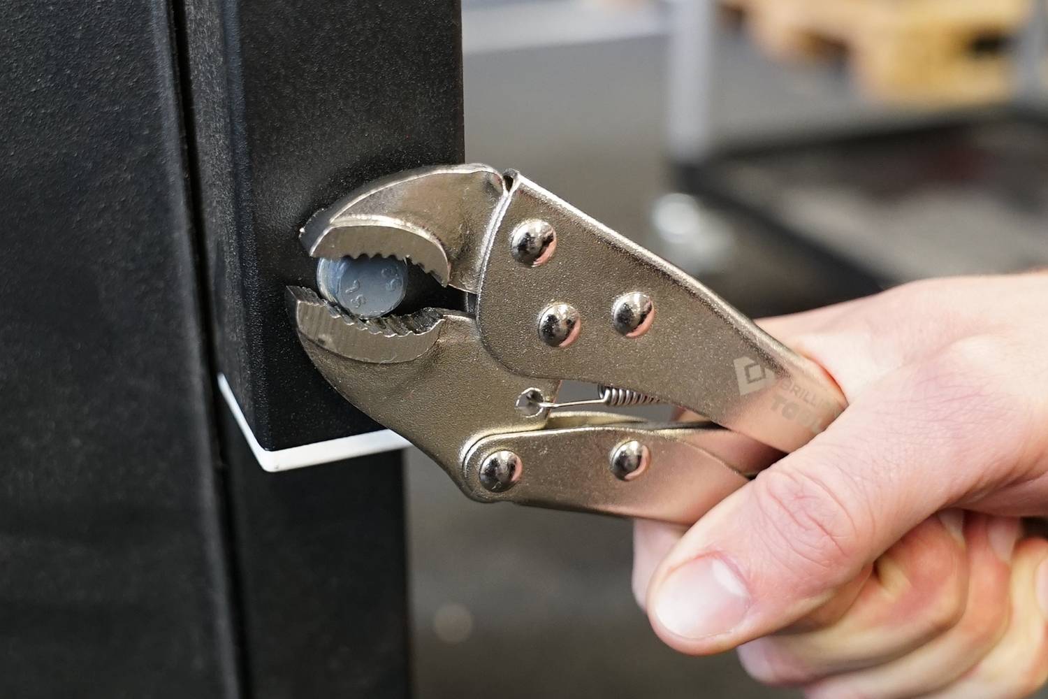 Una mano tiene una pinza a punta che tira un oggetto metallico per aprire o regolare qualcosa.