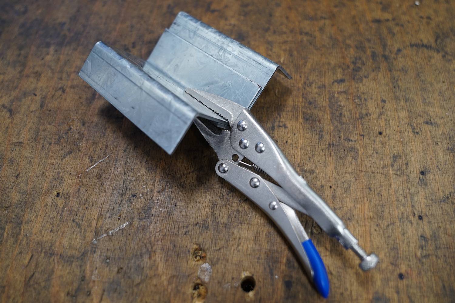 Una pinza di fissaggio tiene un pezzo di metallo curvo su un tavolo di legno, probabilmente per un lavoro di officina.