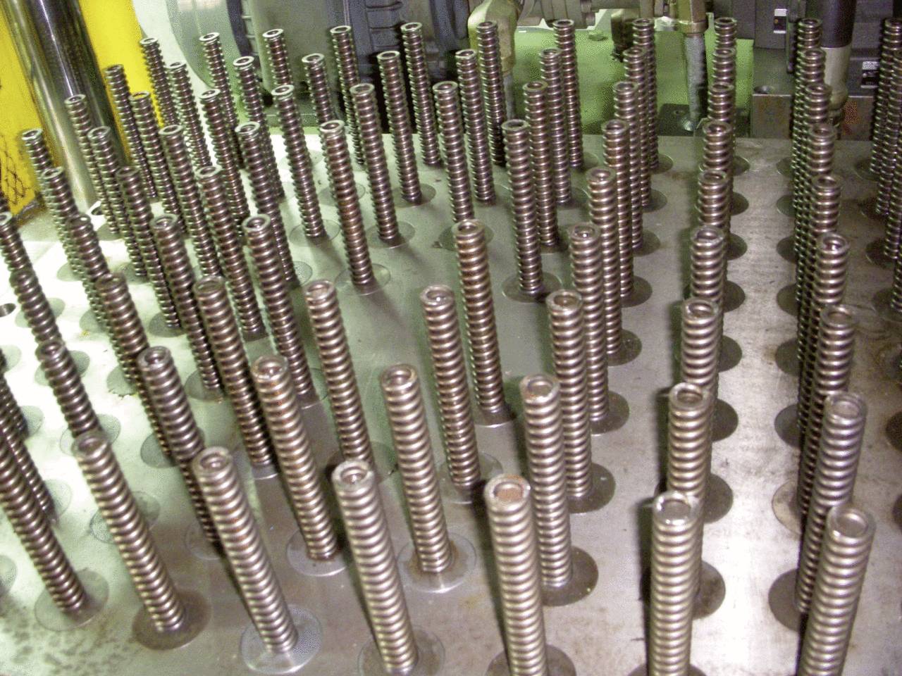 Molle metalliche disposte in più file su un tavolo di macchine, probabilmente parte di un processo di fabbricazione in uno stabilimento industriale.