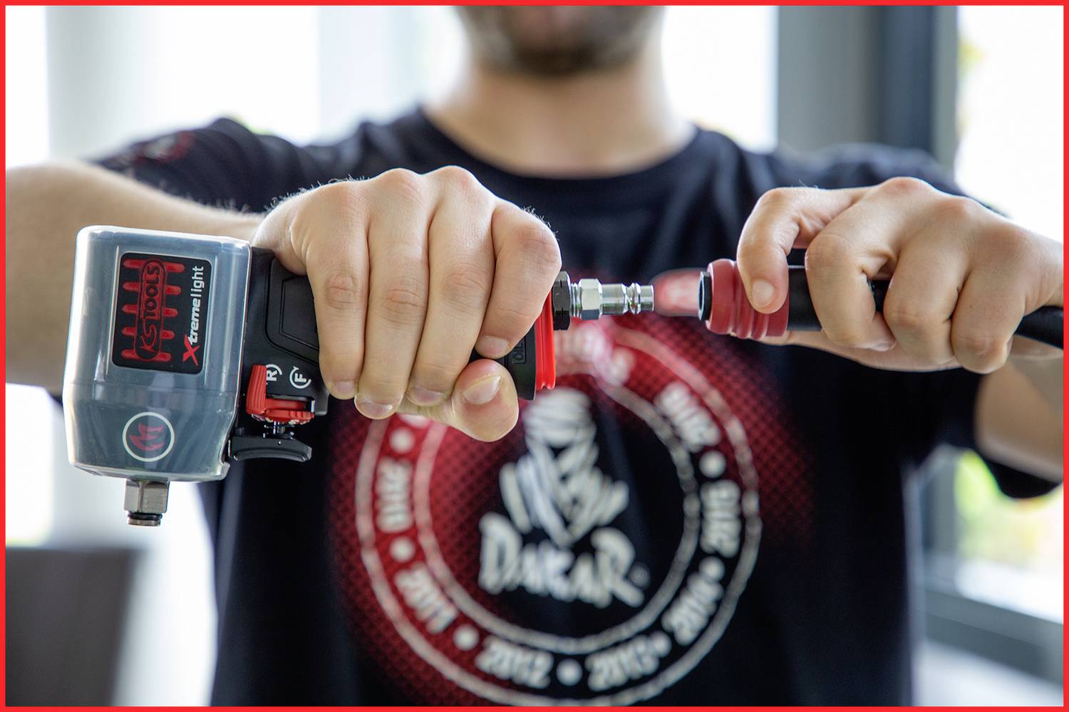 Una persona tiene un utensile pneumatico con entrambe le mani, preparandolo per l'uso. Il motore sullo sfondo è sfocato.