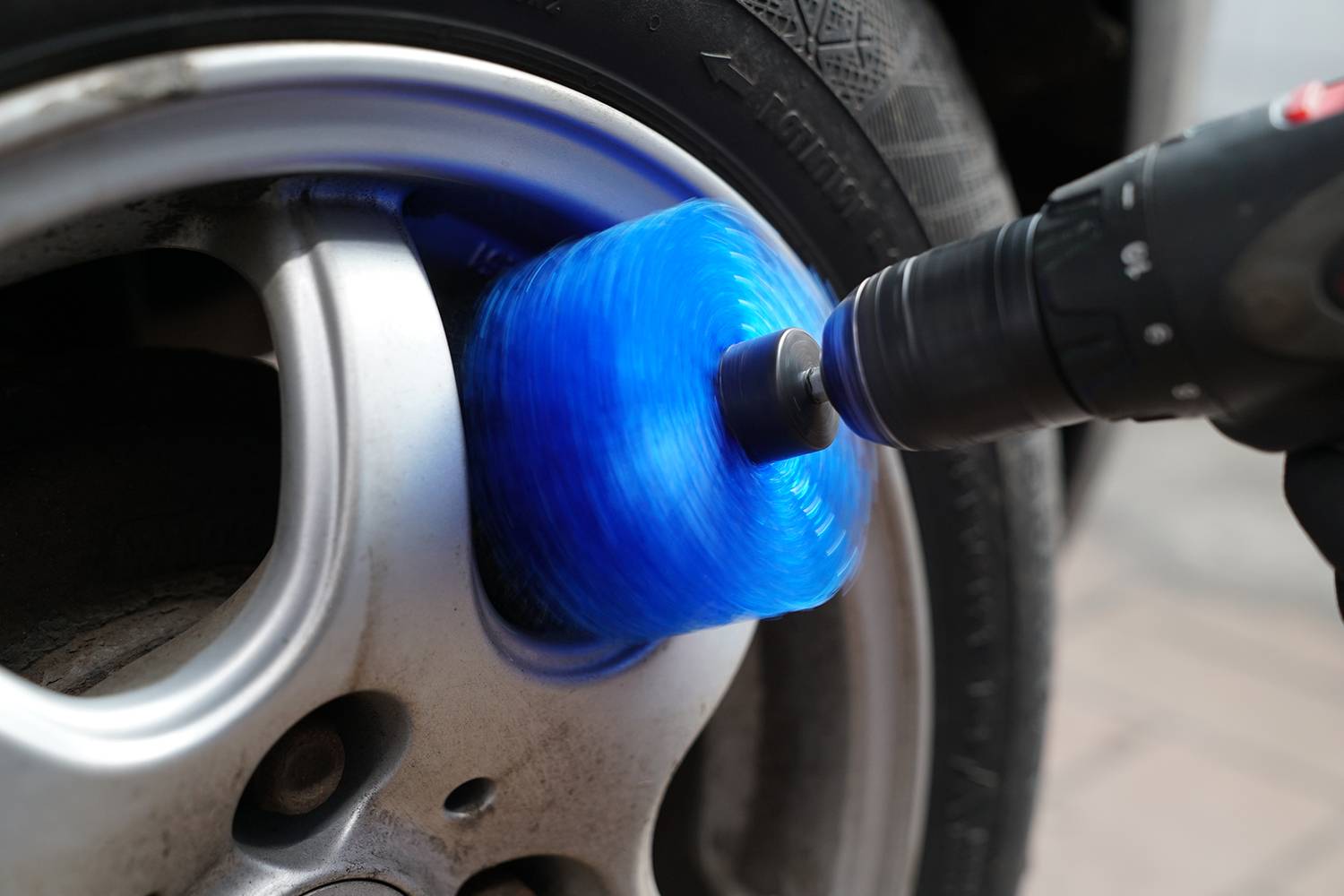 Primo piano di un pneumatico per auto che viene pulito con una spazzola blu su un utensile da trapano. Il cerchio è color argento.