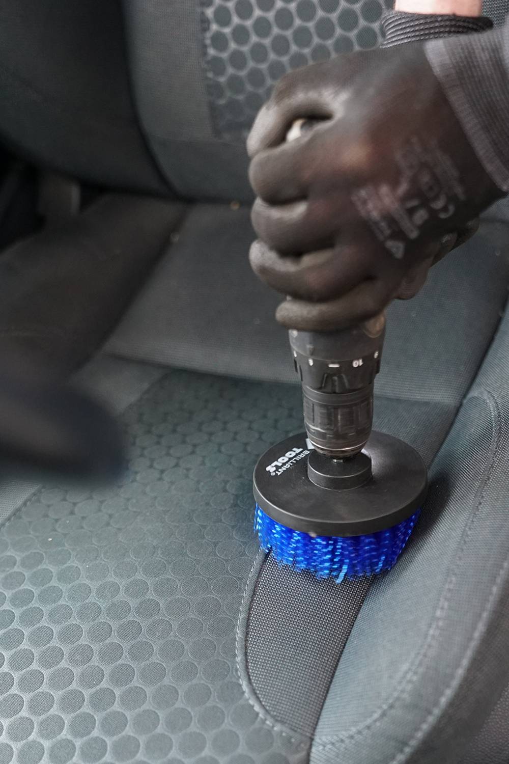 Una persona sta pulendo il sedile di un'auto con una spazzola blu. La spazzola è fissata a un dispositivo.