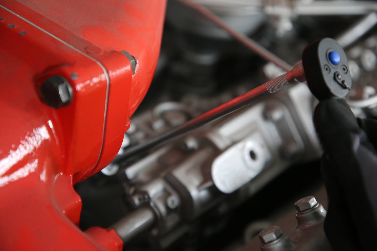 Blocco motore rosso e parti metalliche di un motore di un'auto, parzialmente nascosti da una mano che impugna una chiave inglese.