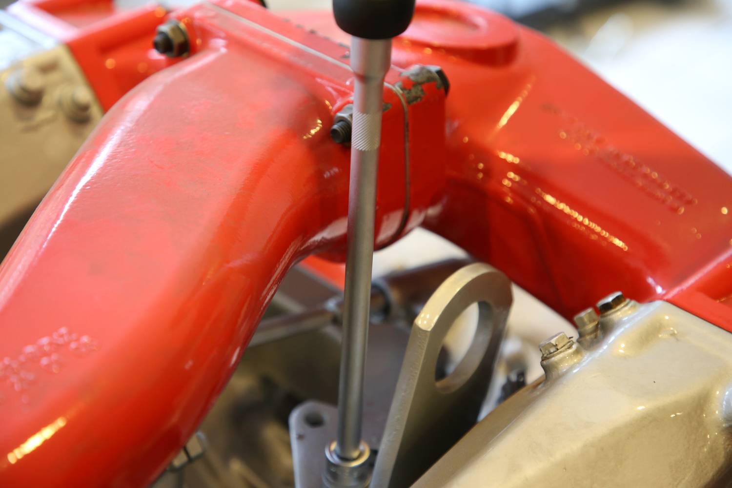 Parte meccanica rossa con leva, presumibilmente parte di un motore o di un componente meccanico. Focus sulla leva e sui punti di fissaggio.