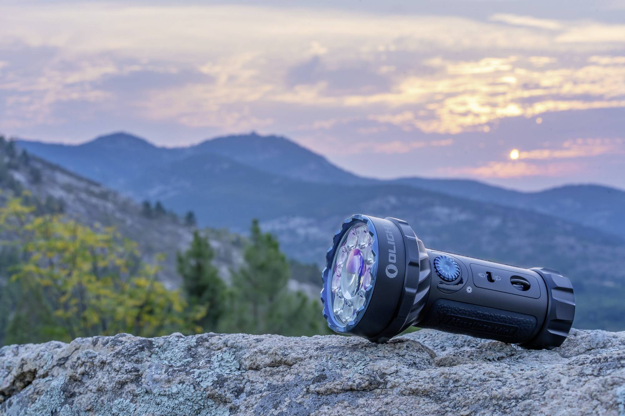 Una torcia elettrica è poggiata su una roccia al tramonto in un paesaggio montano. Il cielo mostra nuvole e luci colorate.