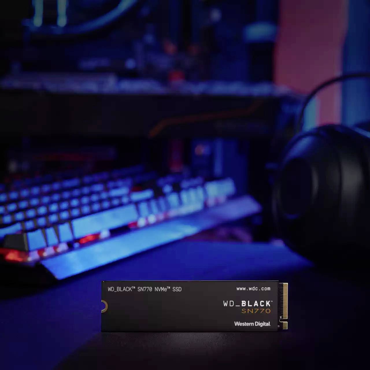 Un'SSD NVMe davanti a un setup da gaming illuminato con tastiera e cuffie, evidenziata in primo piano.