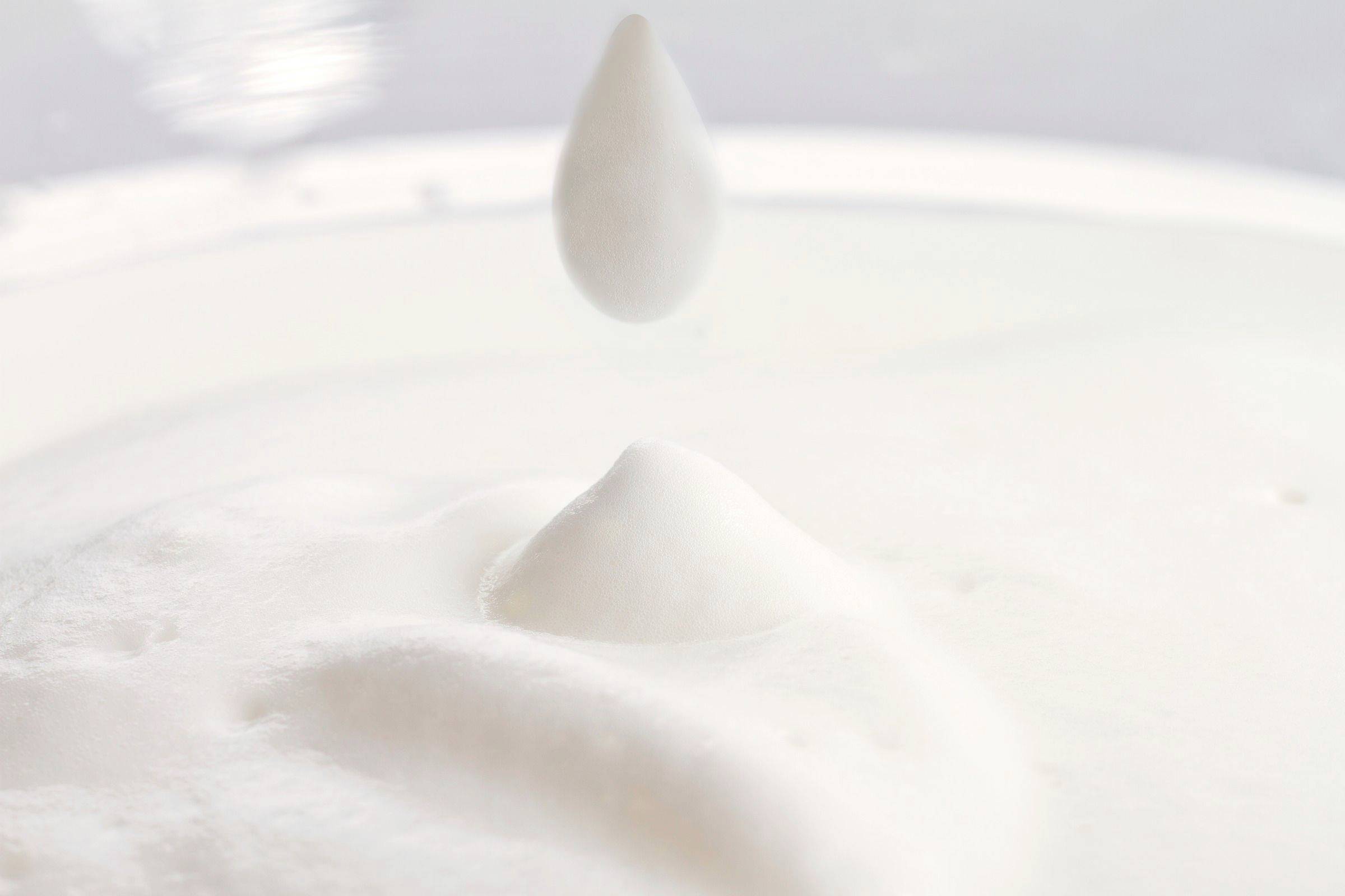 Una goccia cade in una sostanza liquida bianca, causando onde e una piccola punta.