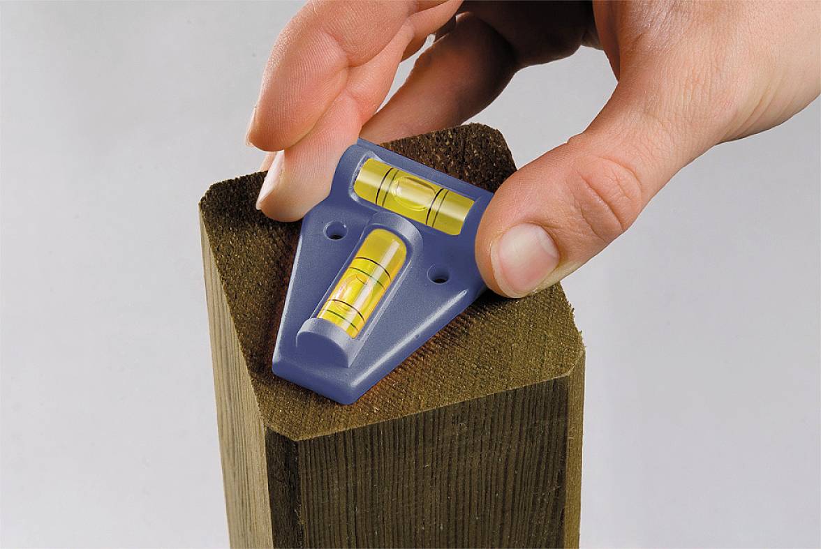 Una mano regge una livella blu su un travetto di legno. La livella mostra se il travetto è allineato orizzontalmente e verticalmente.