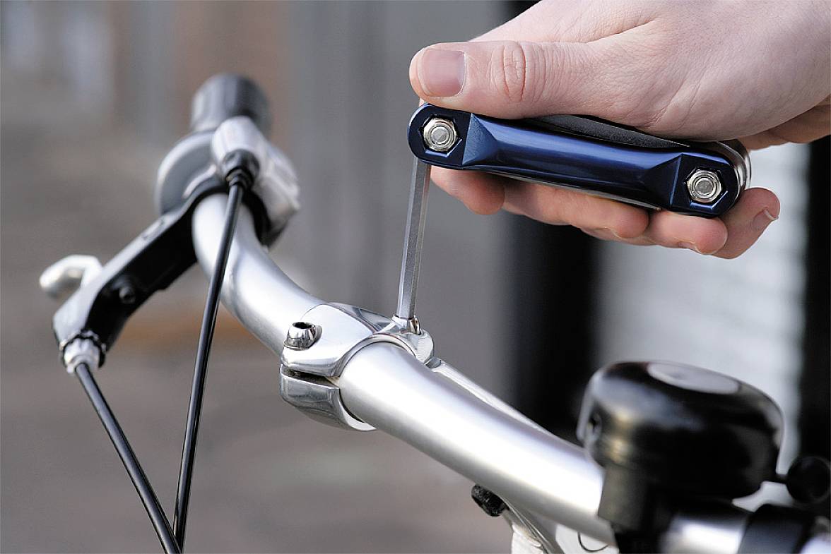 Una mano regola il manubrio della bicicletta con una chiave a brugola; focus sullo strumento e sul fissaggio del manubrio.