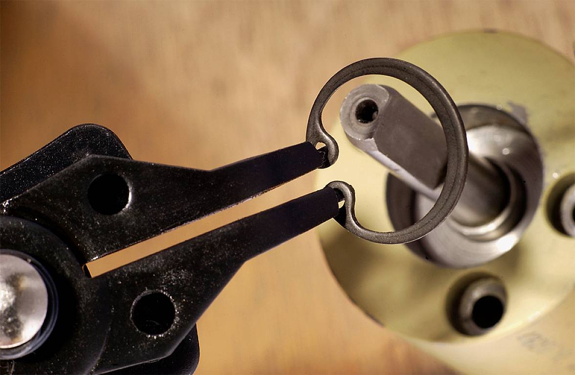 Due pinze nere tengono un anello di sicurezza accanto a un tubo metallico e un dispositivo giallo. Focus sulla riparazione o assemblaggio.