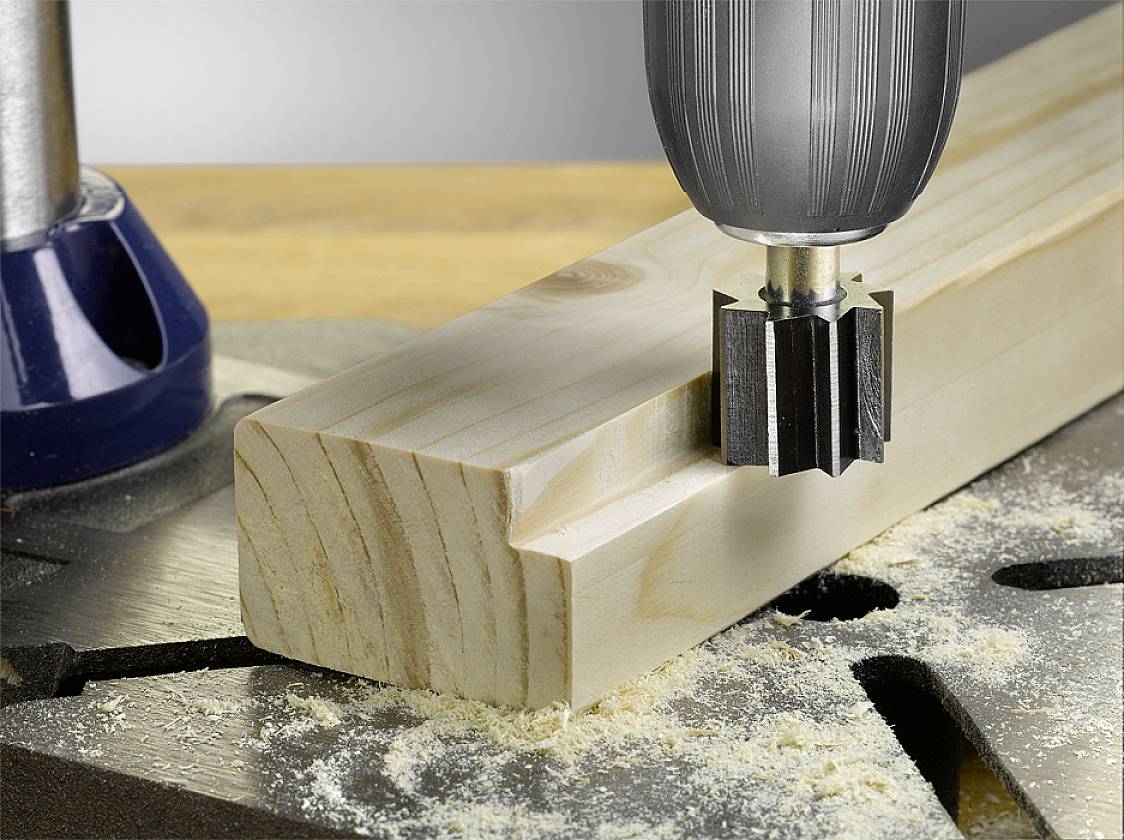 Un tornio CNC lavora con precisione un blocco di legno. La fresa crea una scanalatura, mentre i trucioli di segatura sono sparsi sul piano di lavoro.