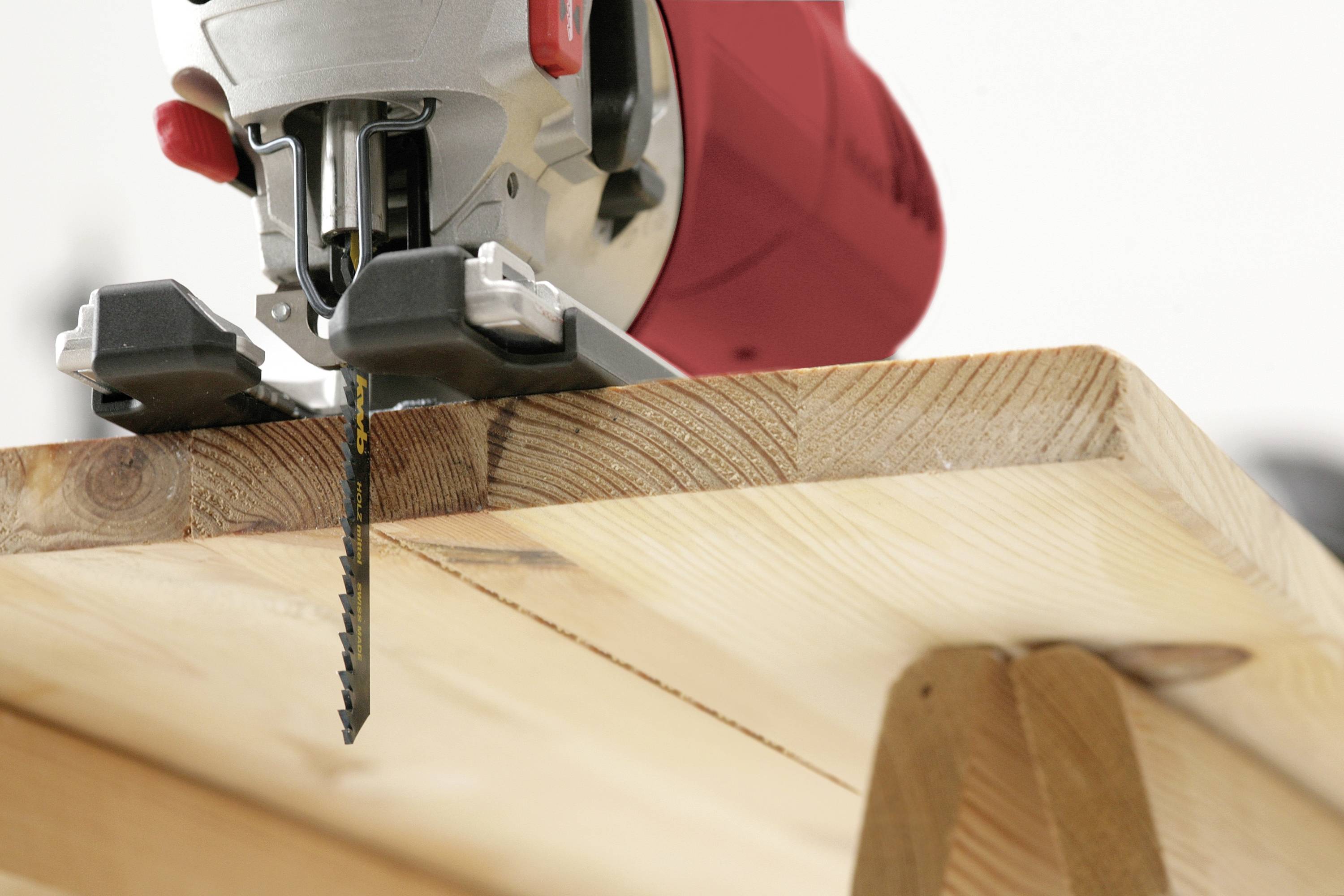Primo piano di un seghetto alternativo che taglia un pezzo di legno da una superficie di lavoro.