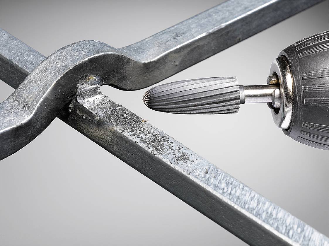 Un trapano rettifica barre metalliche. Un primo piano mostra i dettagli dello strumento e della superficie lavorata.
