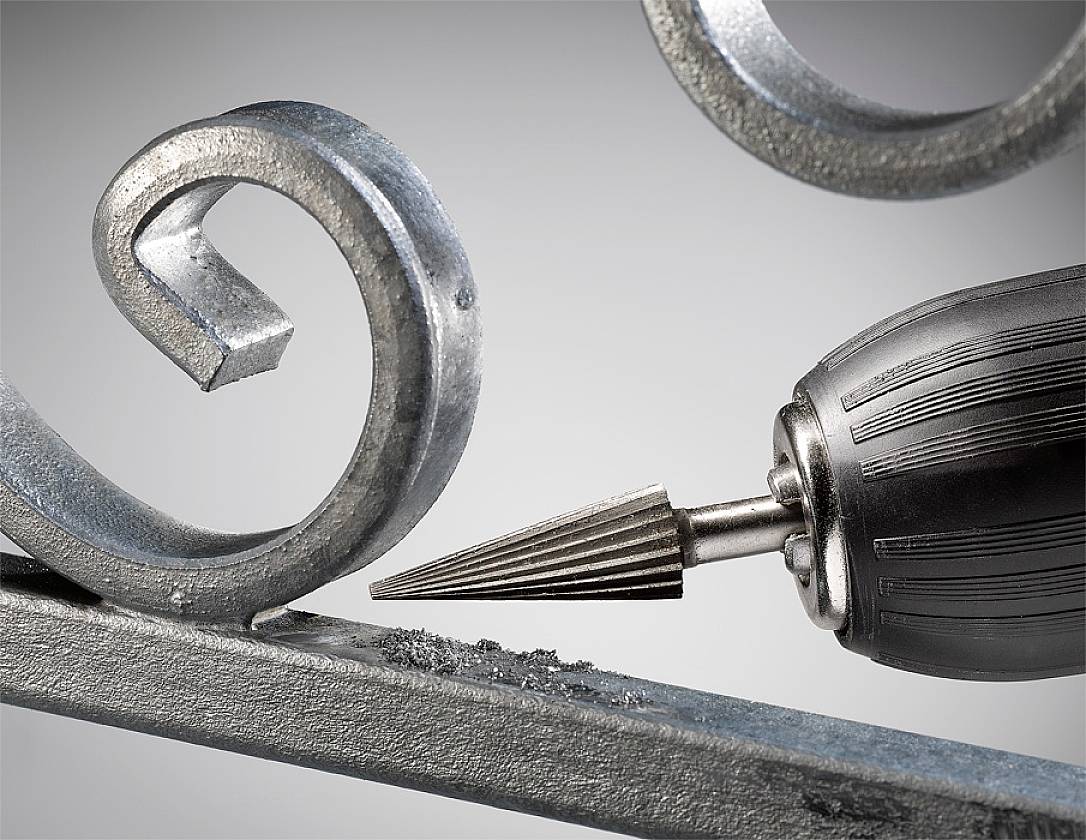 Trapano con fresa a cono lavora un pezzo di metallo con una decorazione a spirale, trucioli metallici visibili. Primo piano che mostra un lavoro preciso.