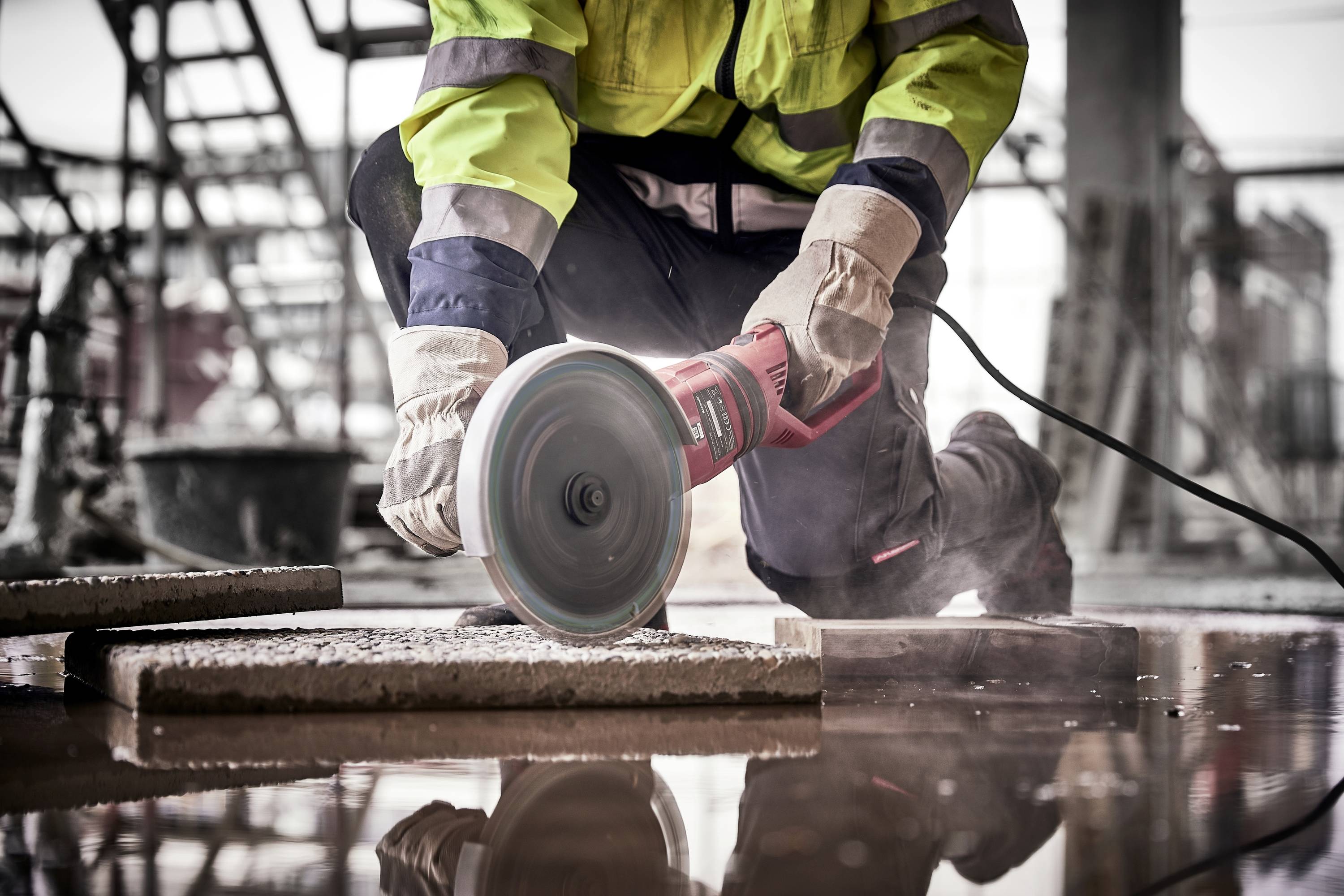 Un lavoratore taglia piastrelle in un cantiere utilizzando un disco da taglio elettrico, indossando indumenti protettivi.