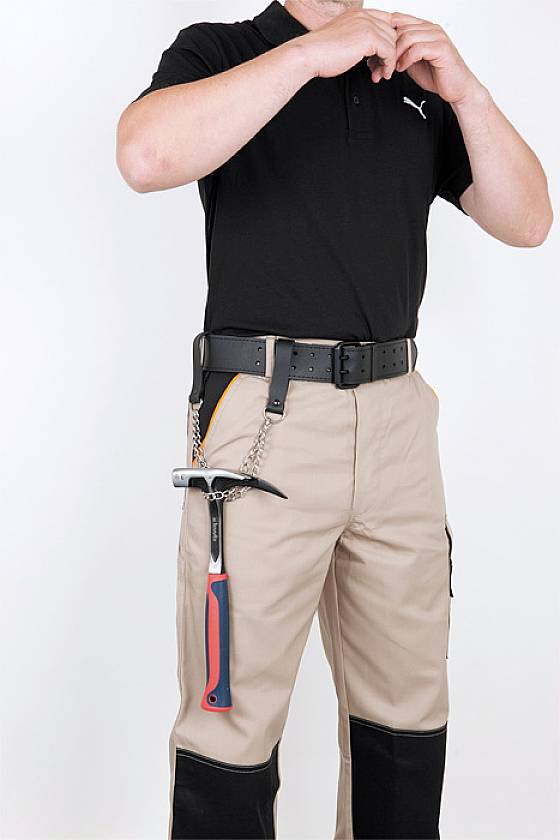 Un uomo in abbigliamento da lavoro, con pantaloni beige e polo nera, sta fissando qualcosa alle sue mani. Un martello pende dalla cintura.