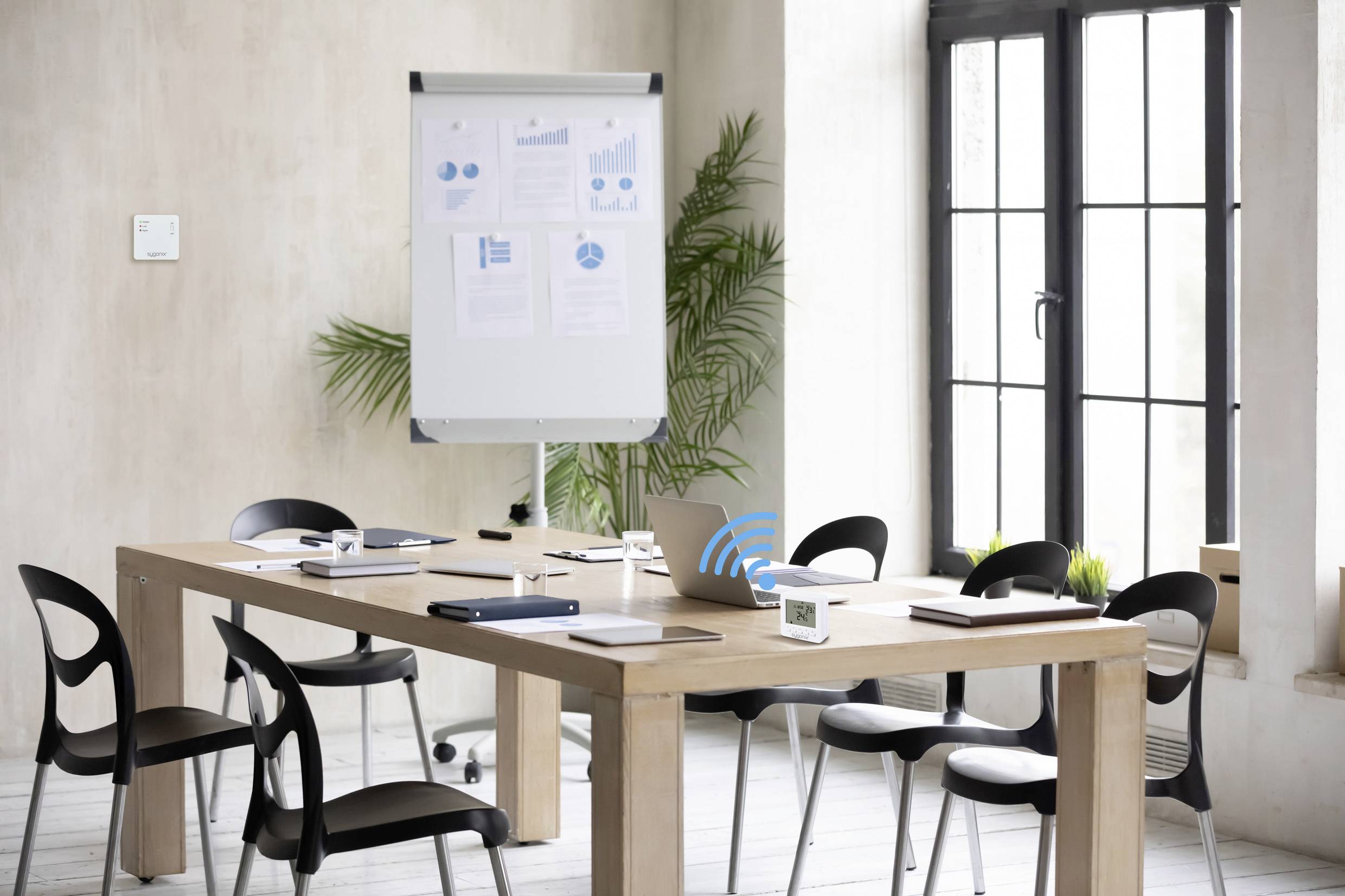 Sala riunioni con un tavolo circondato da sedie. Un flipchart mostra diagrammi. Le finestre sullo sfondo lasciano filtrare la luce.