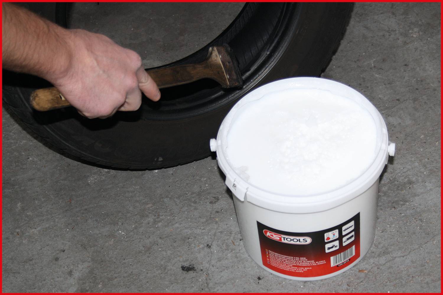Un uomo colpisce un pneumatico con un martello, accanto un secchio di lubrificante.