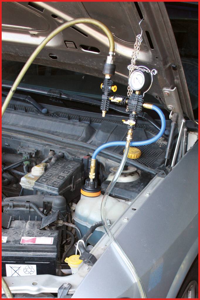 Un vano motore aperto di un'auto con un dispositivo collegato per il controllo del liquido di raffreddamento, che mostra tubi e strumento di misurazione.
