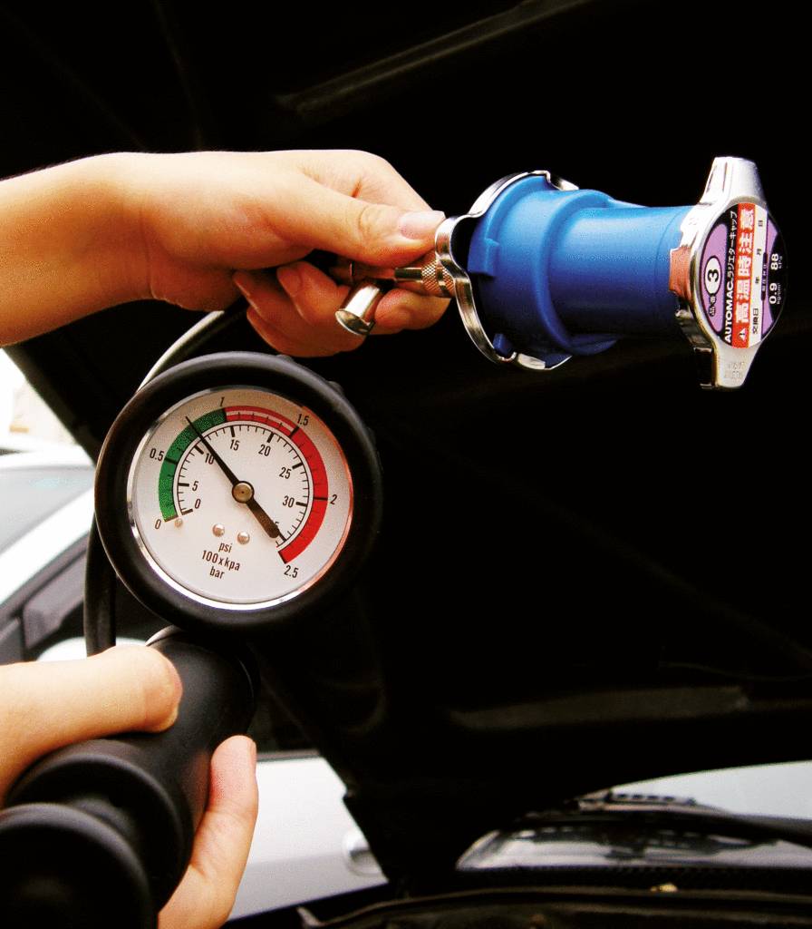 Una persona tiene un manometro e un tester del radiatore per controllare la pressione nel sistema di raffreddamento di un'auto.