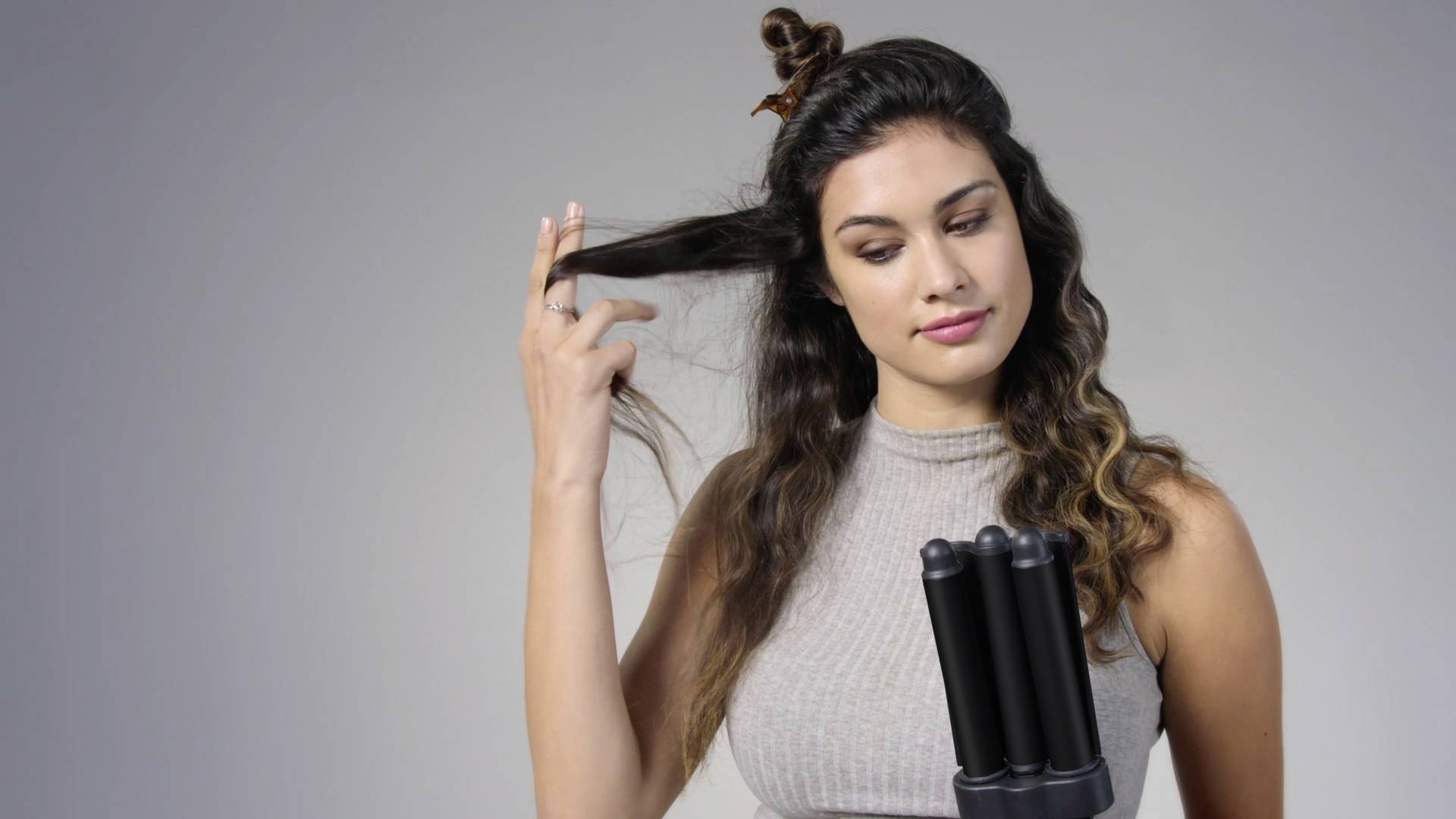 Donna con capelli lunghi utilizza un dispositivo per lo styling con più cilindri rotondi. Tiene una ciocca di capelli per modellarla.