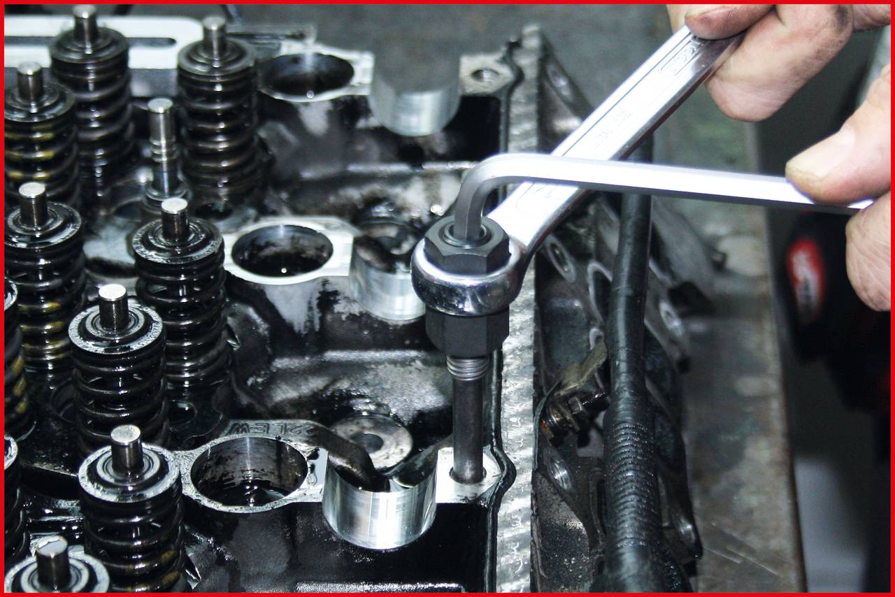 Una persona sta stringendo una vite su un monoblocco motore con una chiave. Le valvole e le molle sono visibili.