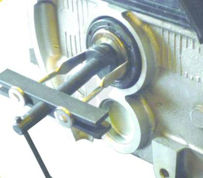 Un estrattore per cuscinetti rimuove un cuscinetto da un asse. Sullo sfondo è visibile una parte dell'involucro metallico.