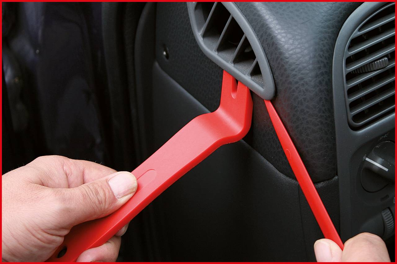 Una persona sta utilizzando utensili in plastica rossa per rimuovere un rivestimento interno dell'auto.