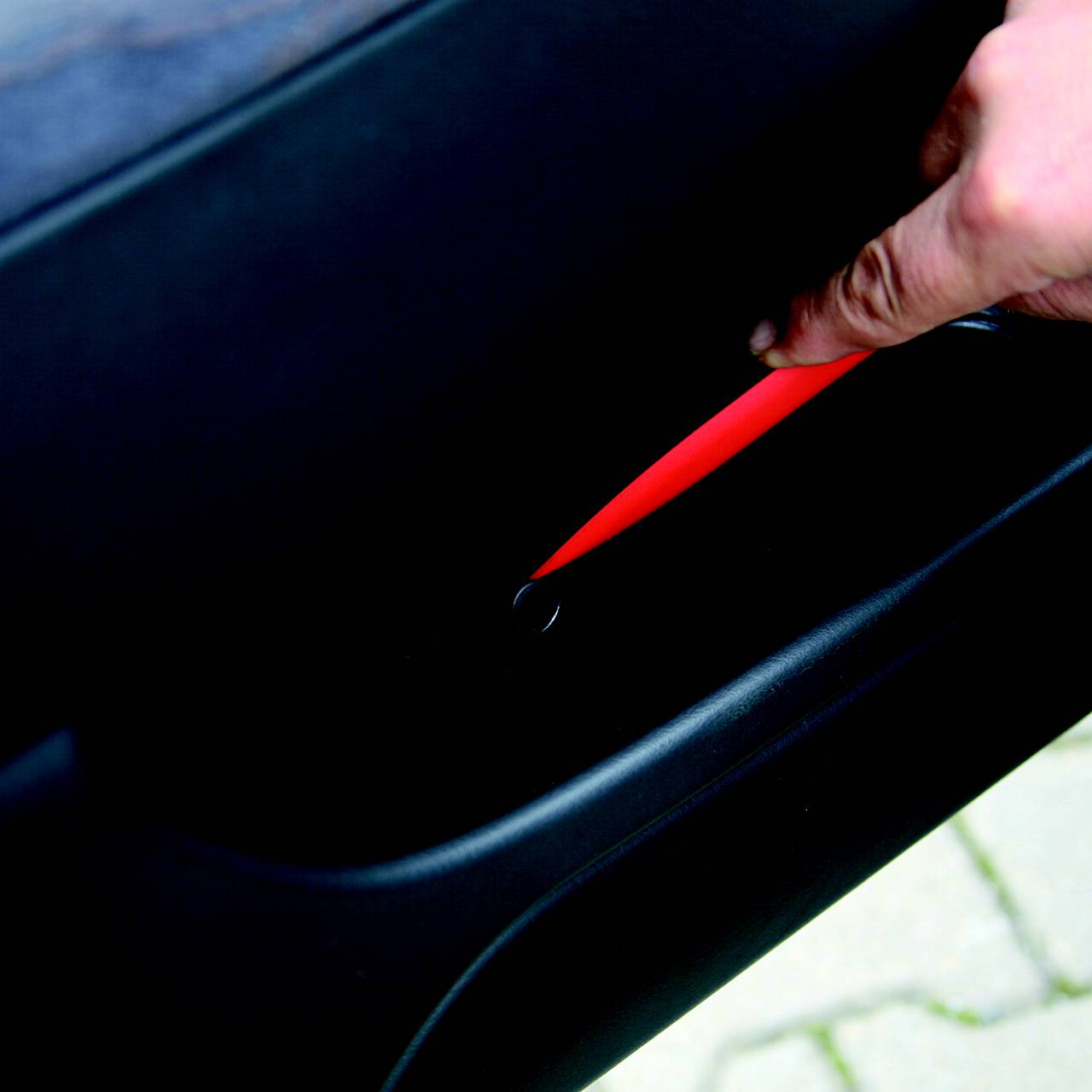Una persona tiene un oggetto rosso in una stretta fessura di un componente auto. Il fuoco è sulla mano e sull'oggetto.