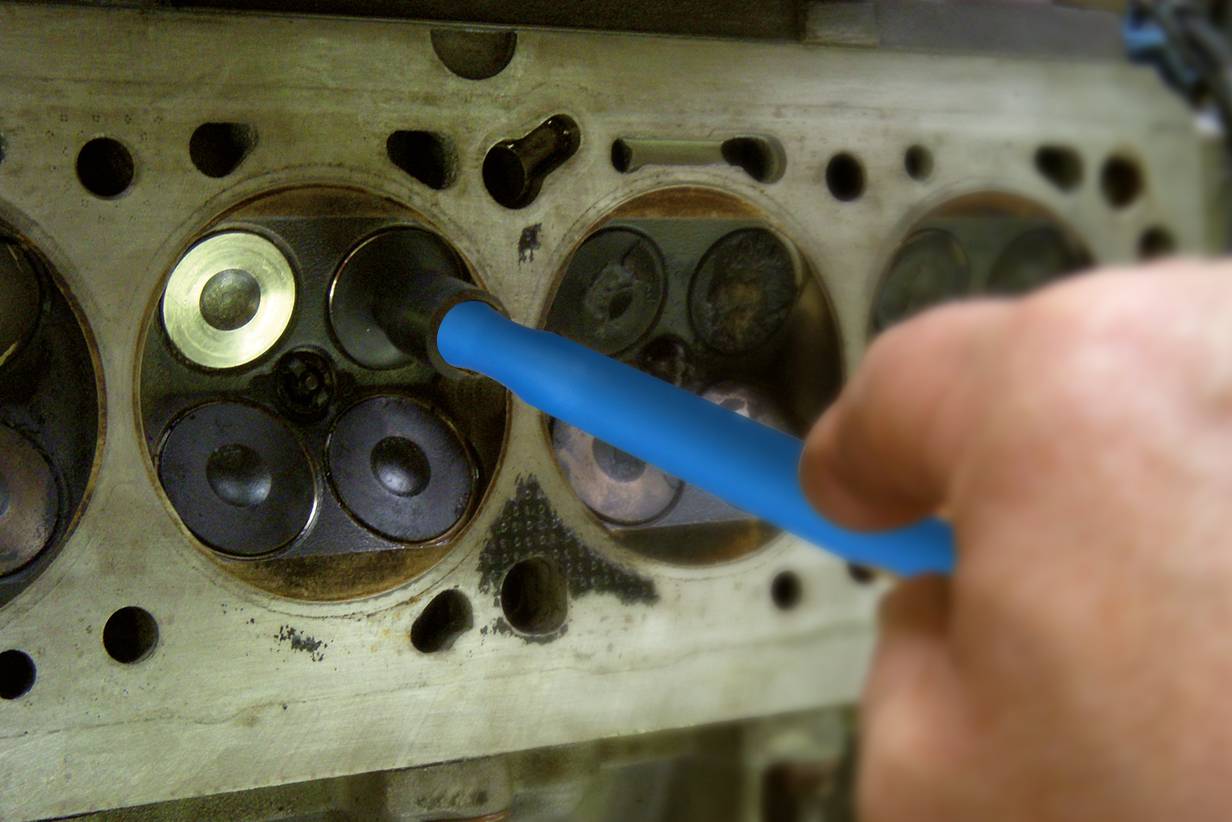 Una mano tiene uno strumento che viene inserito in una testata cilindrica di un motore. Mostra attività di manutenzione o riparazione.