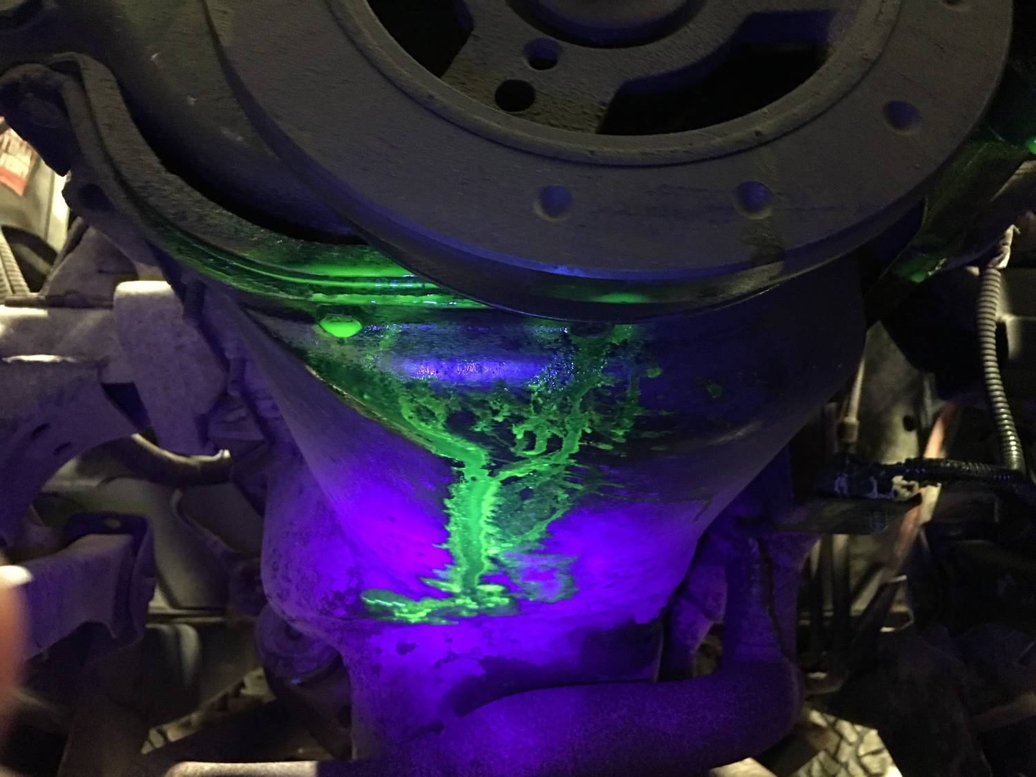 Ricerca di perdite in un motore auto con luce UV: un liquido fluorescente verde indica la fuoriuscita di refrigerante.