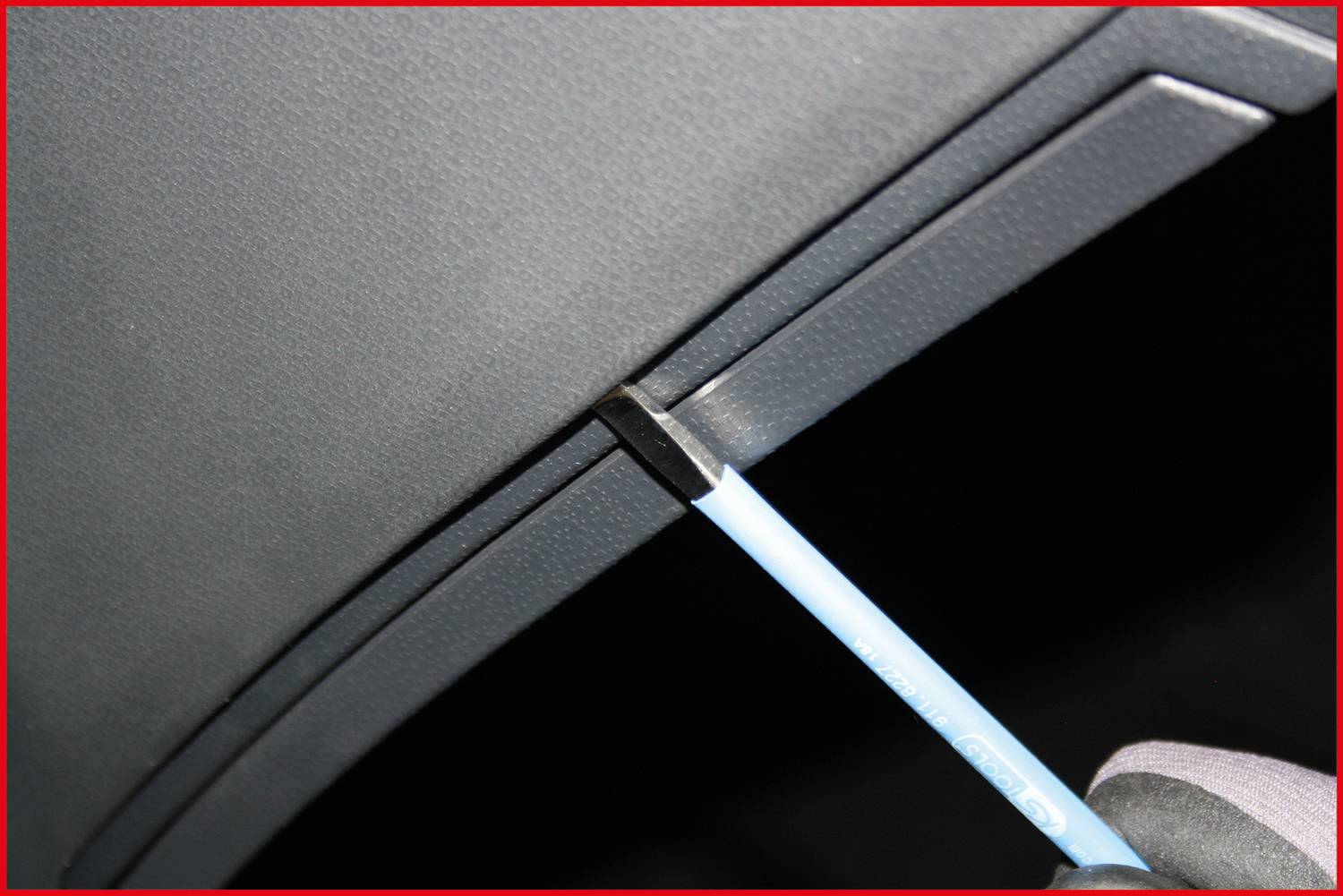 Un cacciavite solleva con cautela un coperchio in plastica all'interno di un'auto, presumibilmente per scopi di riparazione o manutenzione.