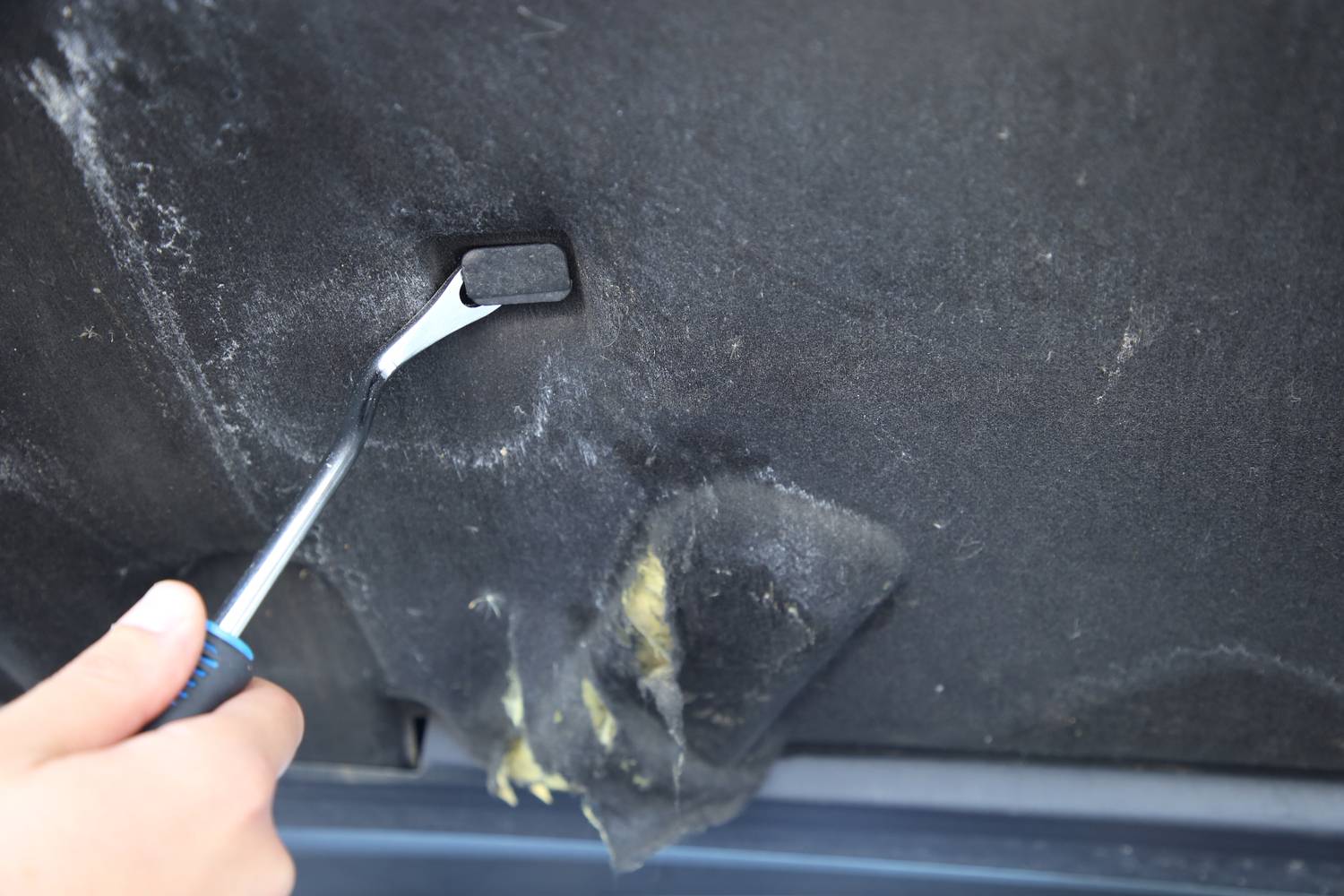 Una persona sta utilizzando un attrezzo per staccare il rivestimento interno di un tetto auto. Il rivestimento è parzialmente allentato.
