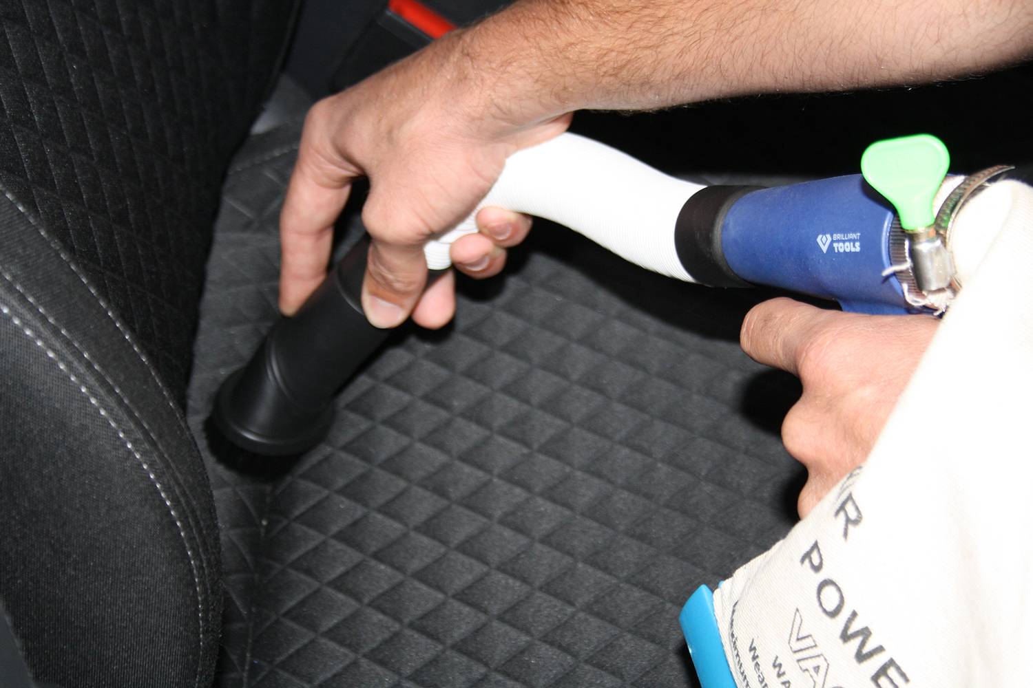 Una persona sta pulendo un sedile dell'auto con un aspirapolvere, con particolare attenzione alla spazzola per imbottiture.
