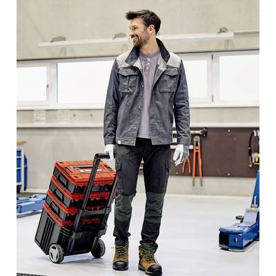 Un uomo in abiti da lavoro è in piedi in un'officina e traina un carrello con contenitori degli attrezzi rossi.