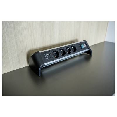 Ciabatta nera con quattro prese e un interruttore, montata su una scrivania contro una parete rivestita in legno.
