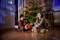 Un bambino e una bambina siedono sorridenti davanti a un albero di Natale splendidamente decorato, tenendo dei regali tra le mani.