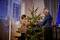 Un uomo anziano e un bambino decorano insieme un albero di Natale illuminato con palline rosse in un accogliente soggiorno.