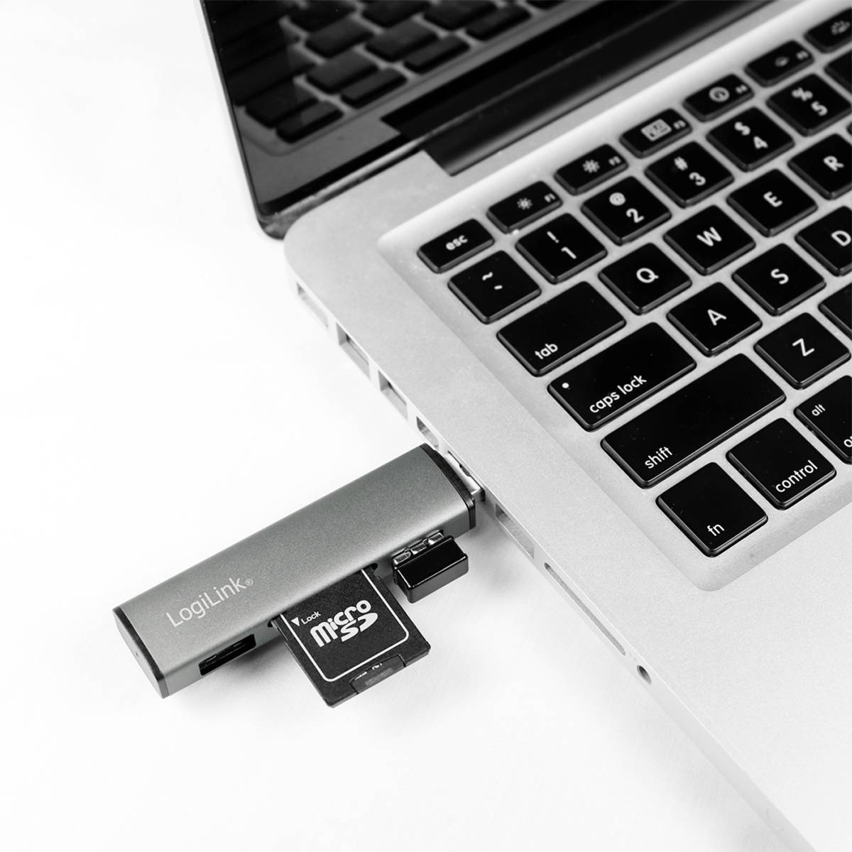 Un lettore di schede MicroSD è collegato a un laptop. L'adattatore ha il logo 'LogiLink' e una scheda MicroSD inserita.
