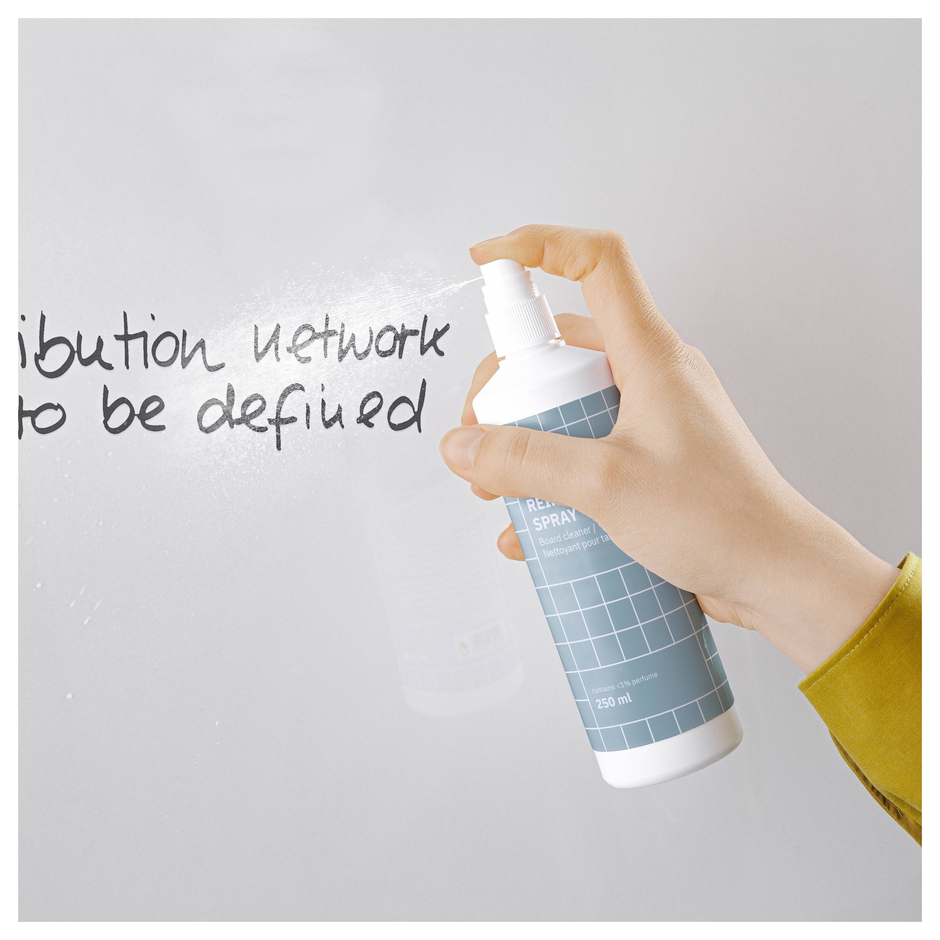 Applicazione di spray detergente con la mano su una superficie in vetro per cancellare testo scritto a mano, con una bottiglia spray blu visibile.