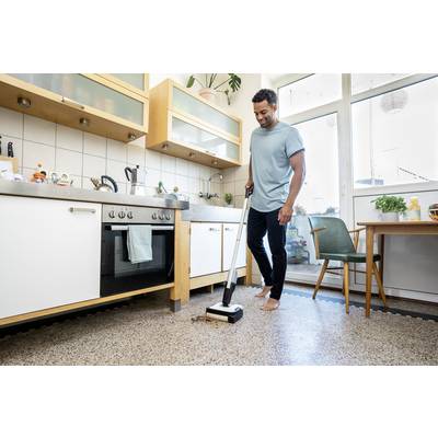 Una persona sta pulendo un pavimento di cucina con un mocio. La cucina è arredata in modo moderno con mobili in legno e grandi finestre.