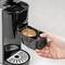Una mano inserisce una capsula di caffè in una macchina per capsule. La macchina e la capsula sono a fuoco, pronte per la preparazione.