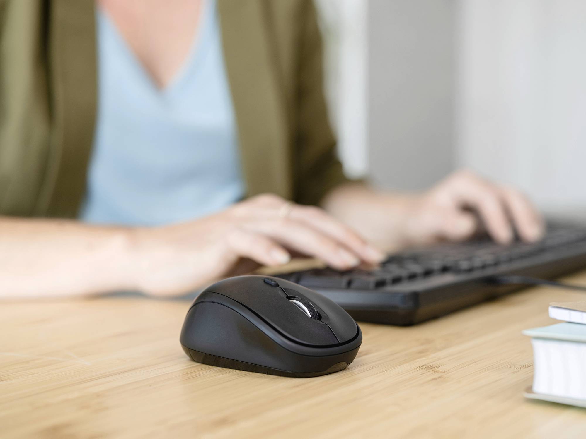 Una persona sta digitando su una tastiera alla scrivania. Accanto a lei c'è un mouse nero.