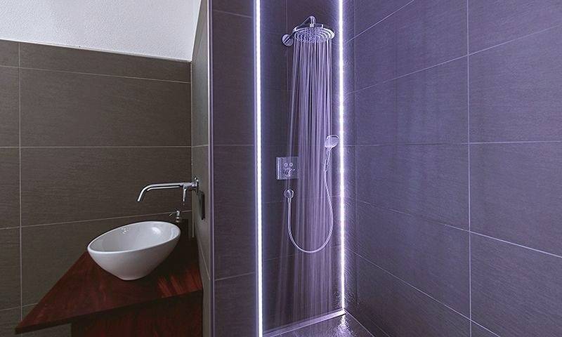 Cabina doccia con acqua corrente e illuminazione a LED, accanto a un lavabo moderno con lavello bianco.